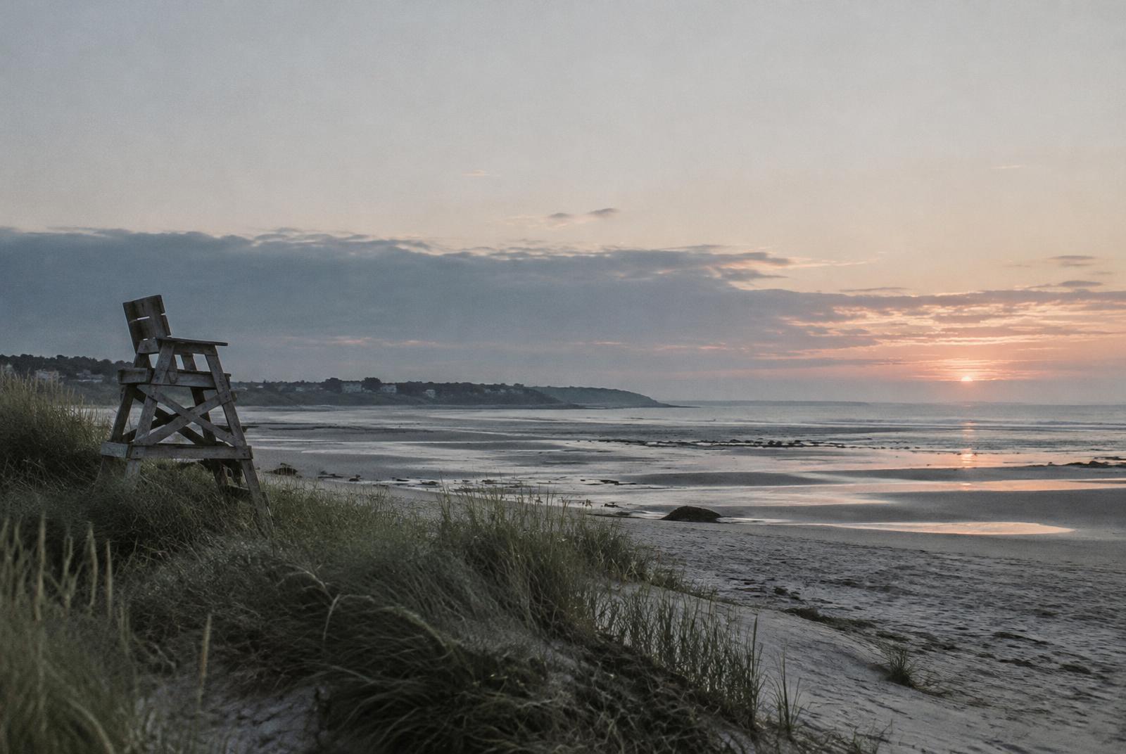 Placeholder: a quiet shoreline at dawn with a wooden lifeguard chair in the dune grass